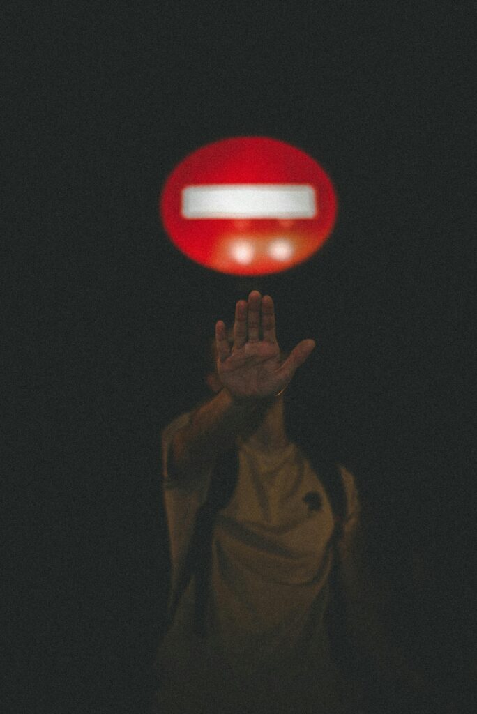A mysterious night scene featuring a person signaling stop beneath a glowing red sign.